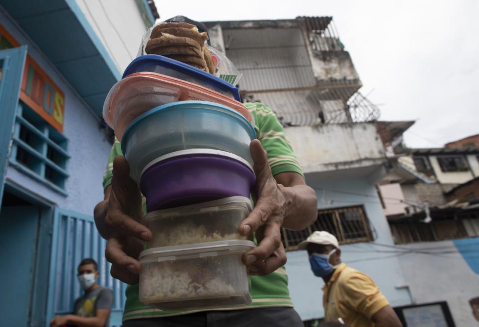 A volunteer carries containers with rice, chicken and salad to be given to residents at the San Antonio de Padua soup kitchen in the Petare neighborhood of Caracas, Venezuela, Thursday, June 10, 2021, amid the new coronavirus pandemic. (AP Photo/Ariana Cubillos)