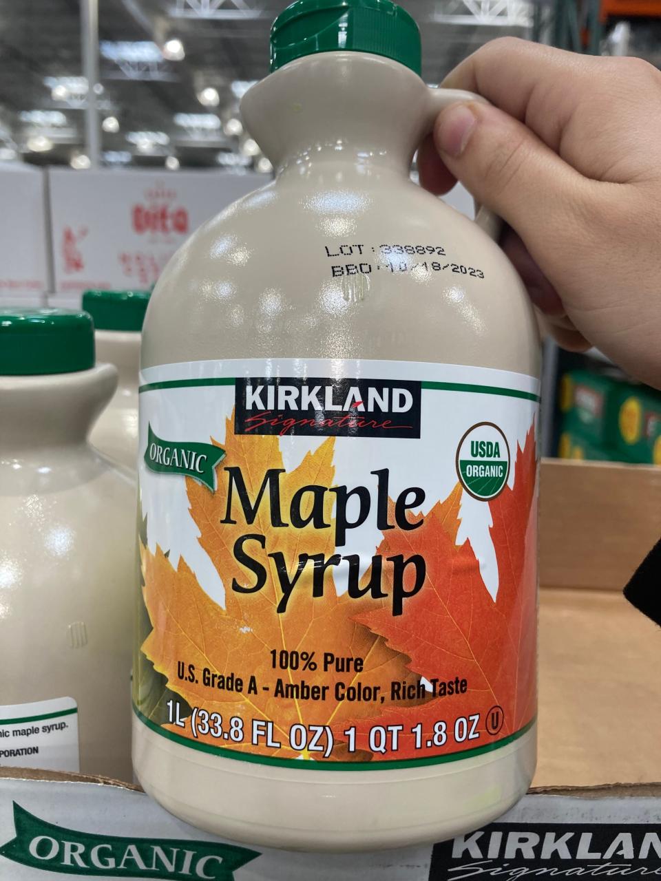 Hand holding a beige jug of maple syrup at Costco