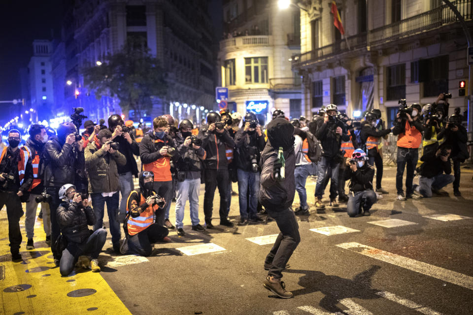 Media take images as a man throws a bottle against a national police station during clashes following a protest condemning the arrest of rap singer Pablo Hasel in Barcelona, Spain, Sunday, Feb. 21, 2021. The imprisonment of Pablo Hasel for inciting terrorism and refusing to pay a fine after having insulted the country's monarch has triggered a social debate and street protests. (AP Photo/Emilio Morenatti)