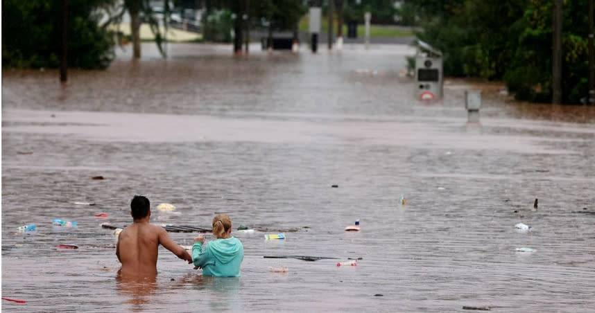 5月2日巴西南大河州，暴雨期間人們洪水氾濫地區行走。（圖／達志／路透社）
