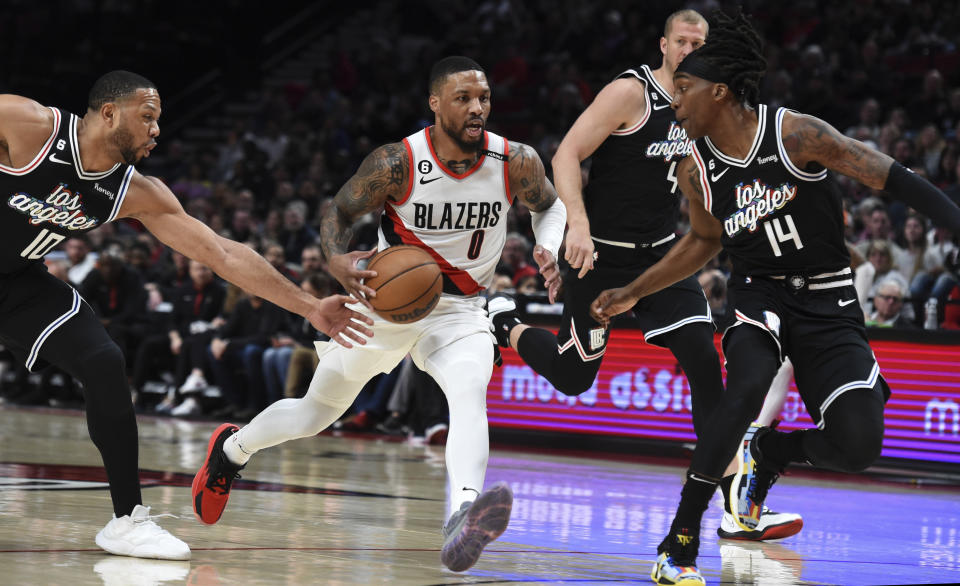 Portland Trail Blazers guard Damian Lillard, center, drives against Los Angeles Clippers&#39; Eric Gordon, left, and Terance Mann, right, during the first half of an NBA basketball game in Portland, Ore., Sunday, March 19, 2023. (AP Photo/Steve Dykes)