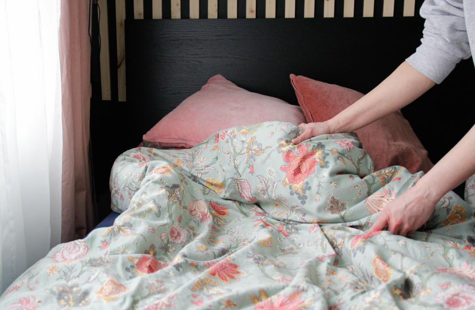 Person making a bed with floral bedding and pillows