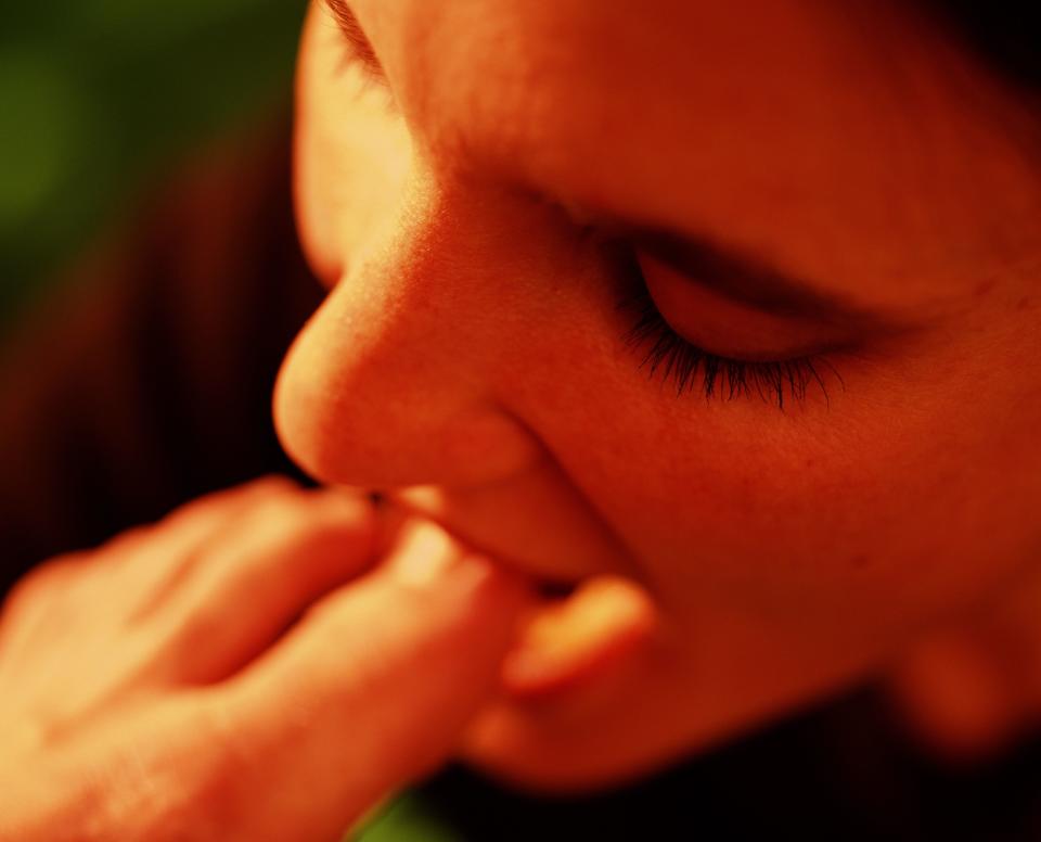 Person eating their own toenail. Their face and closed eye dominate the foreground while the foot is close to their mouth