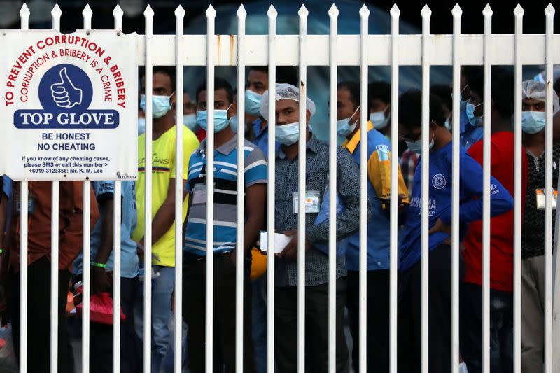 Workers wait in line to leave a Top Glove factory after their shifts in Klang