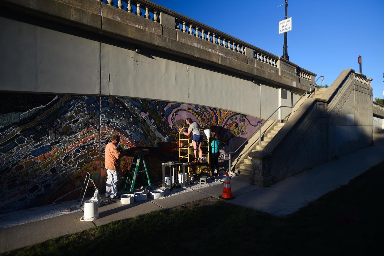 Lansing artist Alexandra Leonard, 35, middle, of Lansing works with volunteers Bob Rose of Lansing and her aunt Anne Leonard of East Lansing as Leonard nears the completion of her "Shiawassee Street Mosaic Project" on the south side of the Shiawassee Street Bridge in downtown Lansing, Thursday, Sept. 29, 2022.