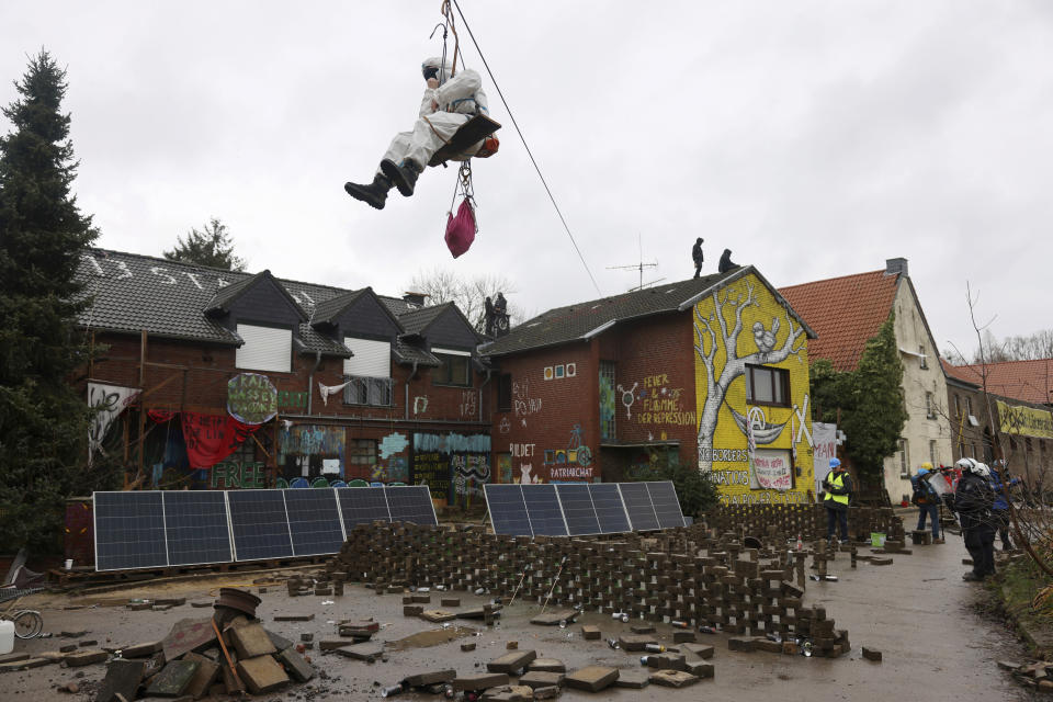 A climate activist hangs from a wire as police officers stand by, right, in a camp of climate protesters in the village Luetzerath near Erkelenz, Germany, Wednesday, Jan. 11, 2023. Police have entered the condemned village, launching an effort to evict activists holed up at the site in an effort to prevent its demolition to make way for the expansion of a coal mine. (Oliver Berg/dpa via AP)