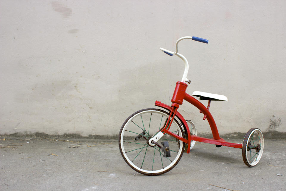 Red Antique Children's Tricycle in front of a Grey Wall.