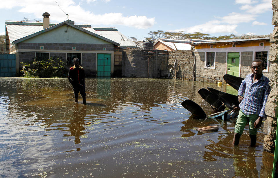 Two people walk outside homes through floodwater that is almost knee-deep.