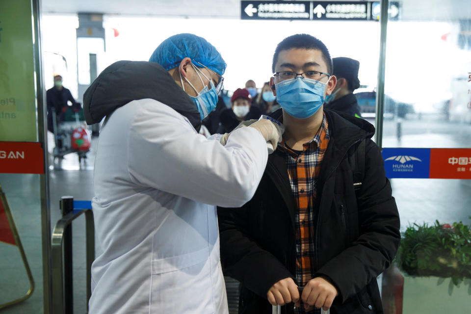 A medical official takes the body temperature of a man at the departure hall of the airport in Changsha, Hunan Province, as the country is hit by an outbreak of a new coronavirus, China, January 27, 2020.  REUTERS/Thomas Peter