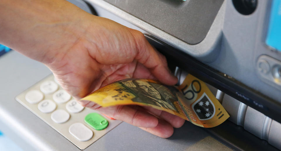 Photo shows a person inserting a $50 note into an ATM.