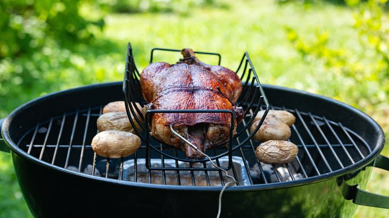 chicken and potatoes smoking on charcoal kettle grill