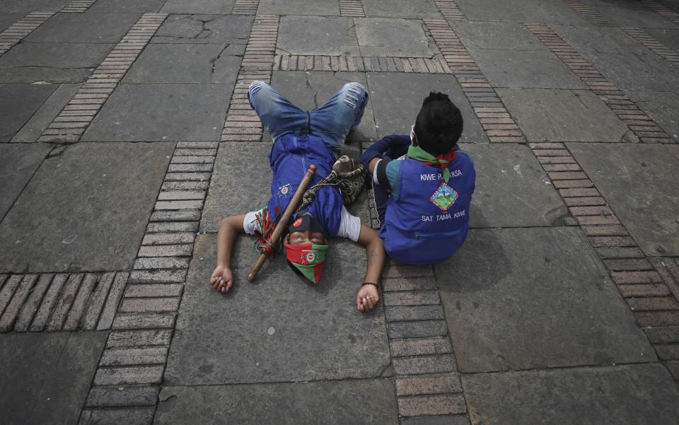 Indigenous men rest after arriving at Bolivar square for a protest against the government in Bogota, Colombia, Monday, Oct. 19, 2020. The leaders of the indigenous communities say they are mobilizing to reject massacres, assassinations of social leaders, criminalization of social protest, to defend their territory, democracy and peace, and plan to stay in the capital for a nationwide protest and strike on Oct. 21. (AP Photo/Fernando Vergara)