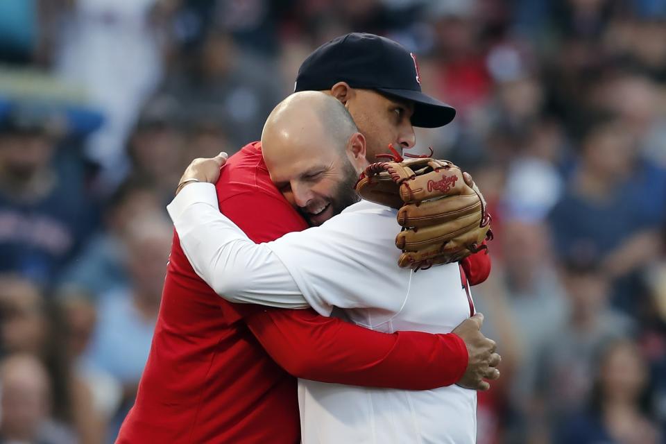 Former Boston Red Sox's Dustin Pedroia, front, hugs manager Alex Cora after throwing out the ceremonial first pitch before a baseball game against the New York Yankees, Friday, June 25, 2021, in Boston. (AP Photo/Michael Dwyer)