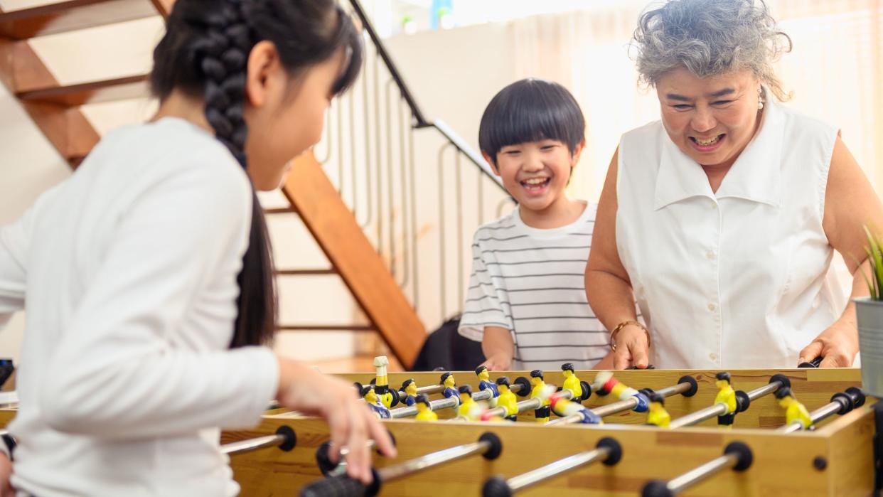 Group of diversity aged family playing soccer table game together happily. Grandmother playing game together with her children at home after retirement daily lifestyle. Happy healthy senior concept.