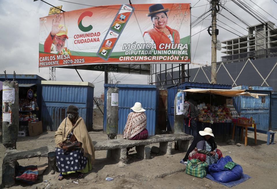 A billboard promoting presidential candidate Carlos Mesa of the Citizen Community political party towers over a trio of women in Rio Seco, Bolivia, Saturday, Oct. 17, 2020. Sunday's presidential election gives Bolivians a chance for a political reset as they struggle with the dramatic costs of the COVID-19 pandemic. (AP Photo/Martin Mejia)