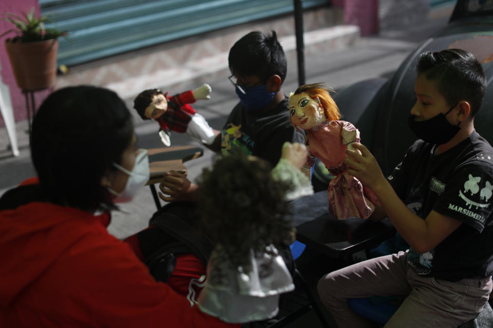 Volunteer Fatima Rodriguez, left, uses puppets to illustrate a history lesson on Spanish colonization and Mexican independence, celebrated in September, to siblings Bryan, right, and Emanuel Quintana, outside the "Tortillerias La Abuela," or Grandma's Tortilla Shop, on the southern edge of Mexico City, Friday, Sept. 4, 2020. Concerned about the educational difficulties facing school-age children during the coronavirus pandemic, the couple who runs the tortilla shop adapted several spaces outside their locale to provide instruction and digital access to locale children who don't have internet or TV service at home, a project which has attracted donations and a waiting list of students. (AP Photo/Rebecca Blackwell)