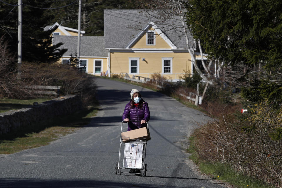 In this Wednesday, May 6, 2020, photo, postmistress Donna DeWitt, wheels the mail to the post office on Isle Au Haut, Maine, an island off the coast. Mail service is essential to many residents who don't play their bills online. (AP Photo/Robert F. Bukaty)