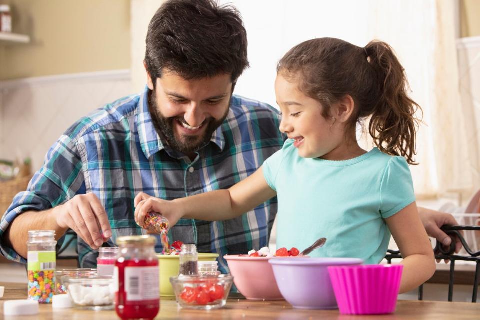 Father and daughter putting sprinkles on ice cream sundaes together. 