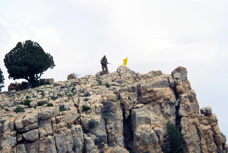 FILE - In this Saturday, May 9, 2015 file photo, a Hezbollah fighter stands on a hill next to the group's yellow flag in the fields of the Syrian town of Assal al-Ward in the mountainous region of Qalamoun, Syria. Aleppo is set to be recaptured by Syrian President Bashar Assad, but the victory will not be Assad's alone. The battle for Syria's largest city has attracted thousands of foreign forces, including Russian soldiers and thousands of fighters from Iran, Lebanon, Iraq and Afghanistan. (AP Photo/Bassem Mroue, File)