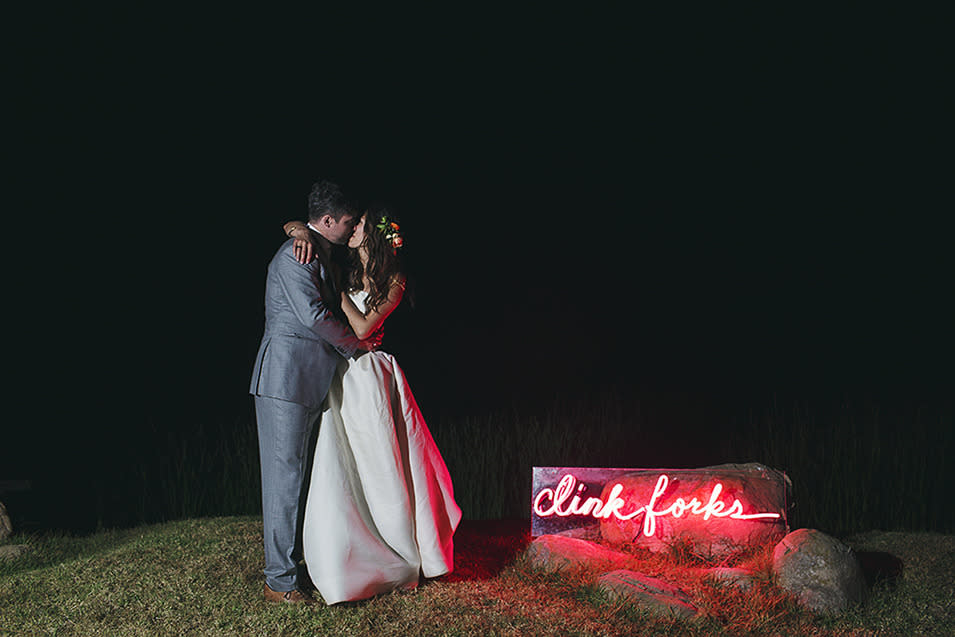 The newlyweds cap off their night with a kiss in front of their custom “Clink forks” neon sign.