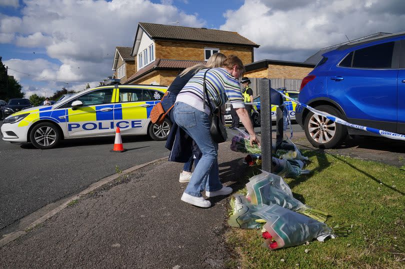 A man and woman deliver floral tributes near to the scene in Ashlyn Close, Bushey, Hertfordshire,