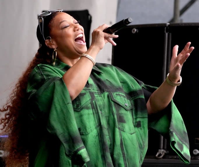 A woman wearing a loose, patterned outfit sings passionately into a microphone during a performance on stage