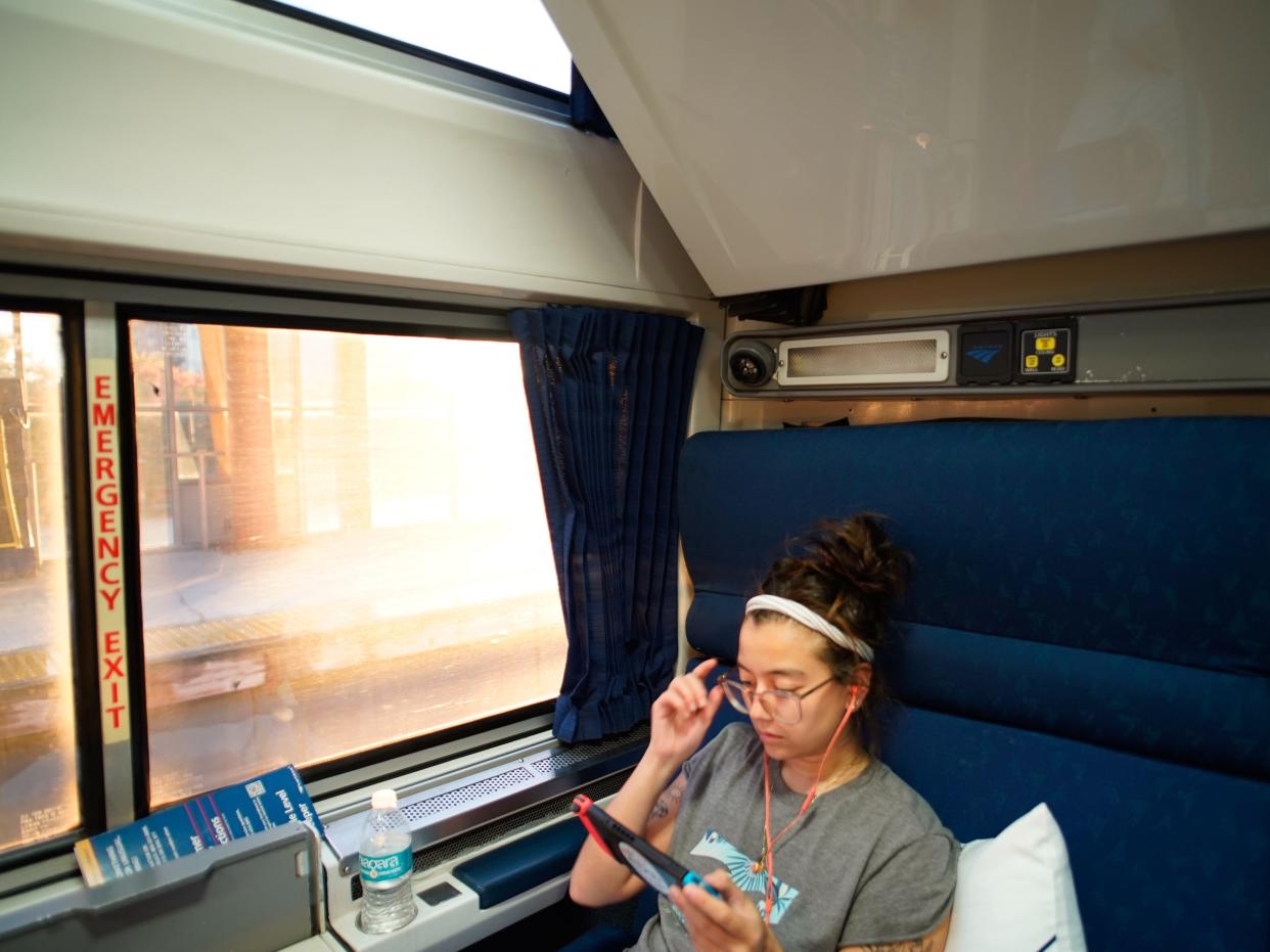 The author sits on the train and plays her Nintendo with the sun peering through the window on the left