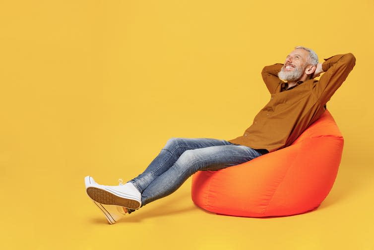 Un hombre sentado en un puf naranja haciendo la posición de lenguaje corporal de catapulta.