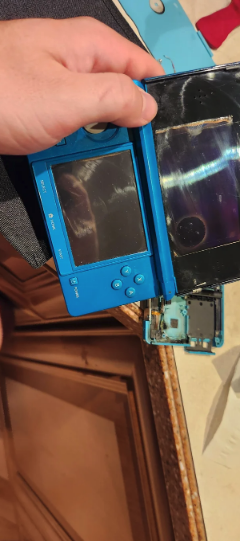 Close-up of a person's hand holding a broken blue handheld gaming console with detached parts. No other text or people are in the image