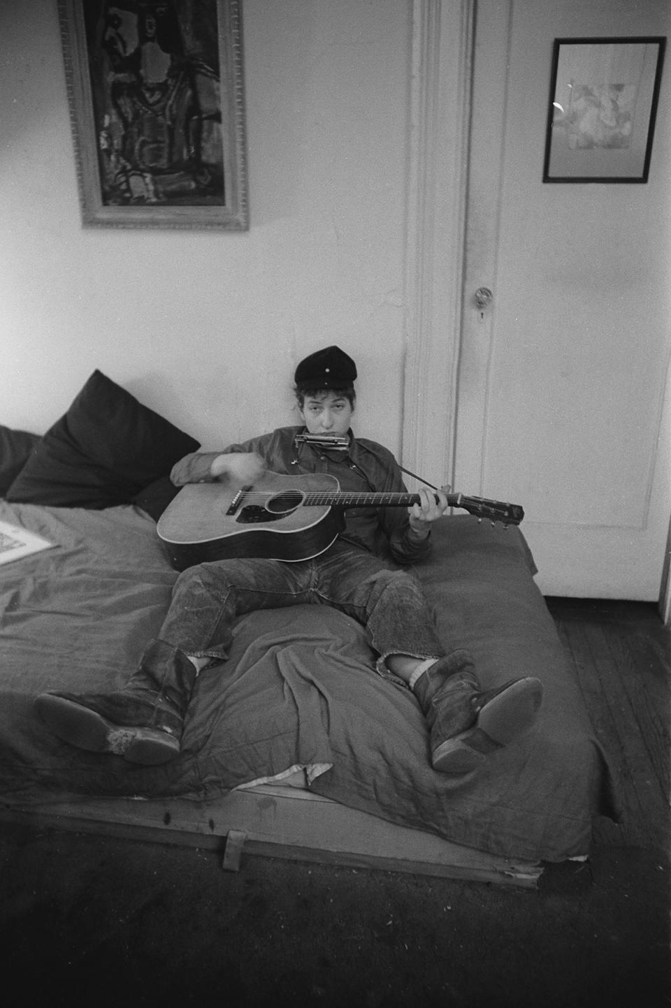 Bob Dylan on bed playing guitar and harmonica