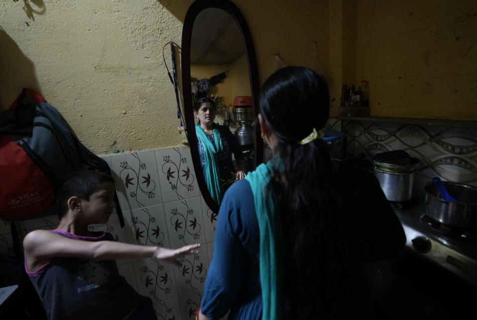 Sheela Singh stands in front of a mirror, with her son playing by her side in Mumbai, India, Sunday, March 19, 2023. When she resigned in 2020 because of pressure from family, her monthly salary was higher than her husband's, an autorickshaw driver whose earnings fluctuated every day — but no one ever suggested he quit. Living in Mumbai on a single salary however has proved too expensive and Singh is now preparing to move back to the village where she once migrated from to live with her parents and enroll her children in school there. (AP Photo/Rajanish Kakade)