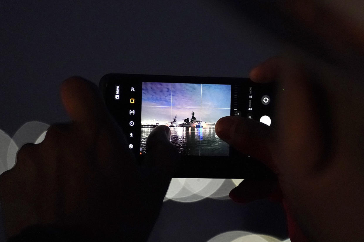 Texas Department of Public Safety Trooper Jose Chapa films the USS Texas with his phone as it is moved away from the dock Wednesday, Aug. 31, 2022, in La Porte, Texas. The vessel, which was commissioned in 1914 and served in both World War I and World War II, is being towed down the Houston Ship Channel to a dry dock in Galveston where it will undergo an extensive $35 million repair. (AP Photo/David J. Phillip)