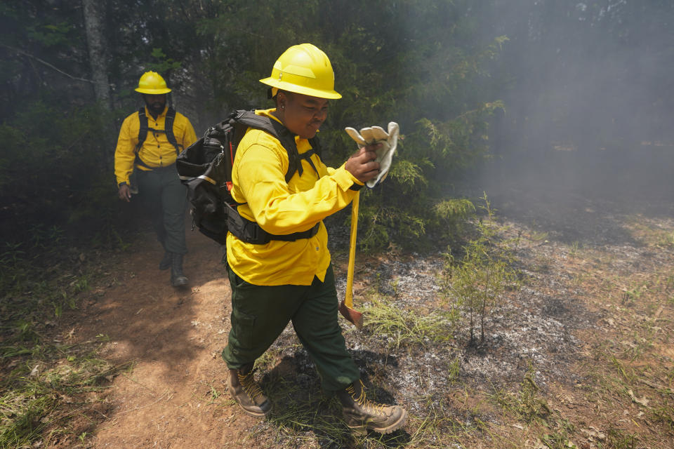 Taylor St. Vilus fans smoke as she walks out of the woods during a wildland firefighter training Friday, June 9, 2023, in Hazel Green, Ala. A partnership between the U.S. Forest Service and four historically Black colleges and universities is opening the eyes of students of color who had never pictured themselves as fighting forest fires. (AP Photo/George Walker IV)