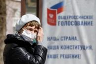 A woman wearing a protective mask near a board informing of a nationwide vote on constitutional changes in Stavropol