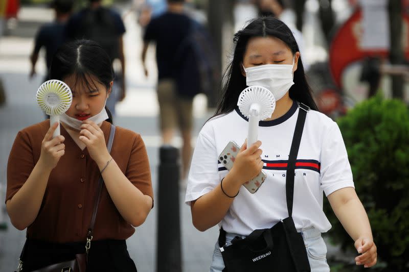 Women wearing masks to prevent the spread of the coronavirus disease (COVID-19) use portable fans to cool down in Seoul