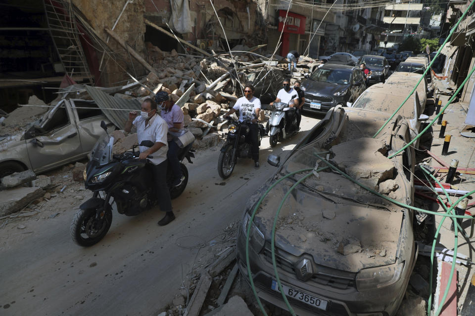 FILE - In this Wednesday, Aug. 5, 2020 file photo, people drive past buildings and cars that were damaged in the Aug. 4 explosion that hit the seaport of Beirut, Lebanon. It was 20 minutes before 6:08 p.m. when the Beirut fire brigade received the call from an employee at the nearby port reporting a big fire. Ten firefighters, including a female paramedic, piled into a fire engine and an ambulance and raced toward the scene, and their ultimate death. (AP Photo/Bilal Hussein, File)