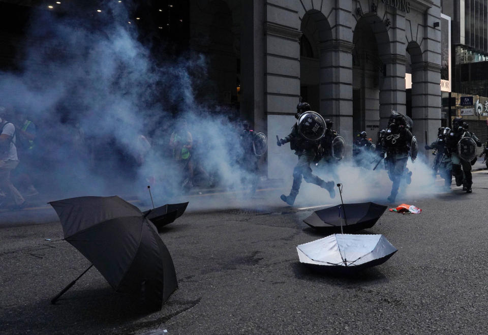 Riot police run past umbrellas abandoned by protesters as tear gas are fired n Hong Kong on Monday, Nov. 11, 2019. A protester was shot by police Monday in a dramatic scene caught on video as demonstrators blocked train lines and roads during the morning commute. (AP Photo/Vincent Yu)          