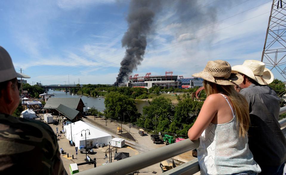 People watch from the Pedestrian Bridge a warehouse fire burns across the river on Saturday in Nashville.