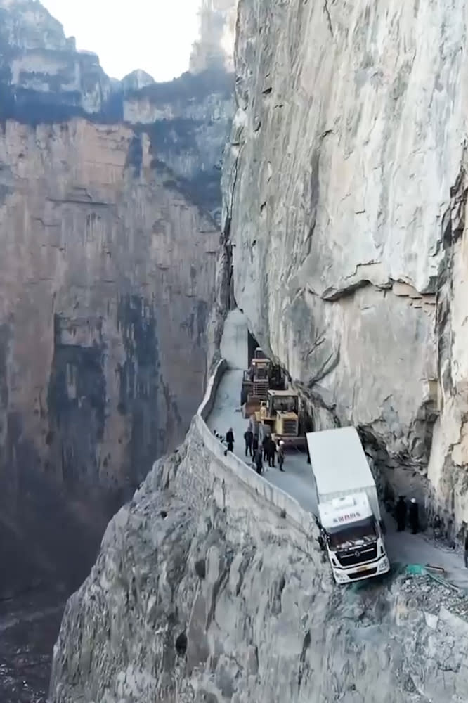 The truck is seen hanging from the steep cliff as cars pile up behind.