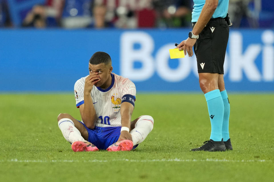 FILE - Kylian Mbappe of France sits on the pitch, hand over his bloody nose, as the referee holds the yellow card, during a Group D match between Austria and France at the Euro 2024 soccer tournament in Duesseldorf, Germany, Monday, June 17, 2024. (AP Photo/Andreea Alexandru, File)