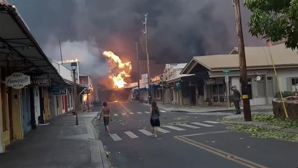 People watch as smoke and flames fill the air from raging wildfires on Front Street in downtown Lahaina, Maui on Tuesday, Aug. 9, 2023. Maui officials say wildfire in the historic town has burned parts of one of the most popular tourist areas in Hawaii. County of Maui spokesperson Mahina Martin said in a phone interview early Wednesday says fire was widespread in Lahaina, including Front Street, an area of the town popular with tourists. (Alan Dickar via AP)