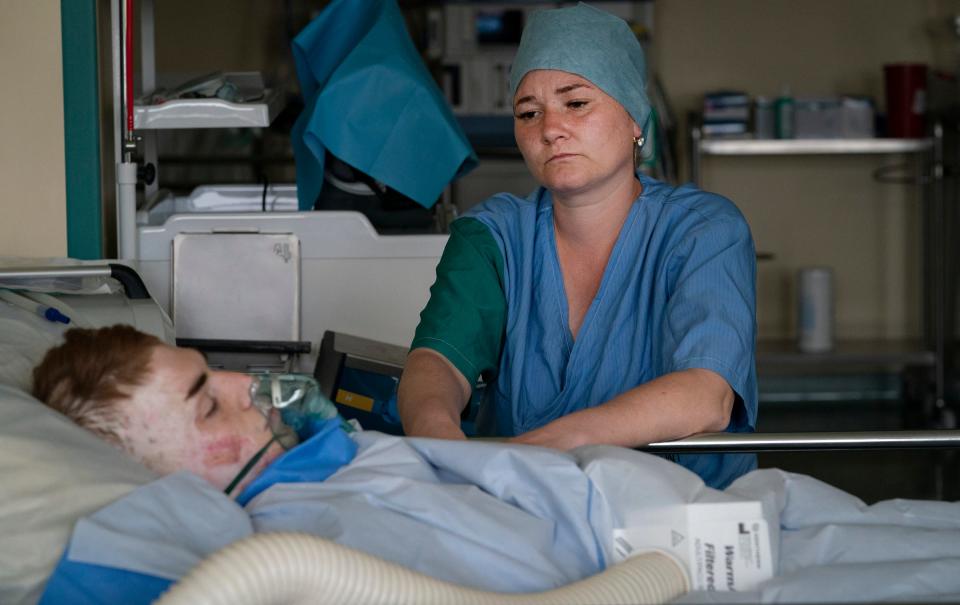 Volodymyr Bubela, 17, of Lviv, Ukraine, left, rests in the recovery room after surgery on his hands as his mother Mariia Kit sits by his side at the Public Health Care Facility in Leczna, Poland on Tuesday, May 16, 2023. Bubela was injured in a barn fire when he was 7 but continues to grow out of his scar tissue requiring updated surgeries.