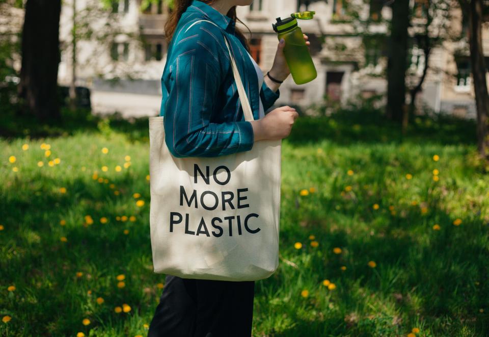 Woman holding reusable cotton zero waste bag with text that says "No More Plastic."