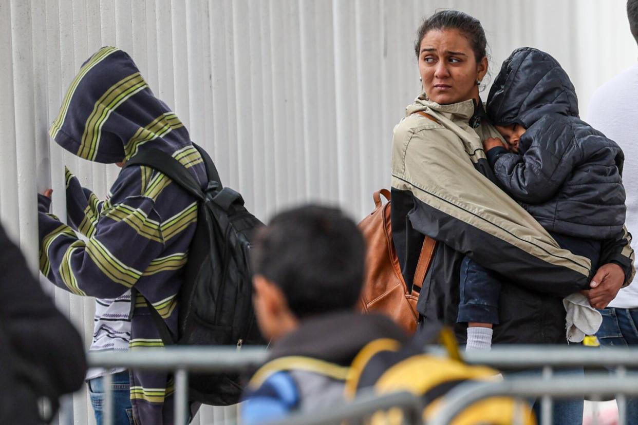 People wait near metal barricades, including a woman holding a child