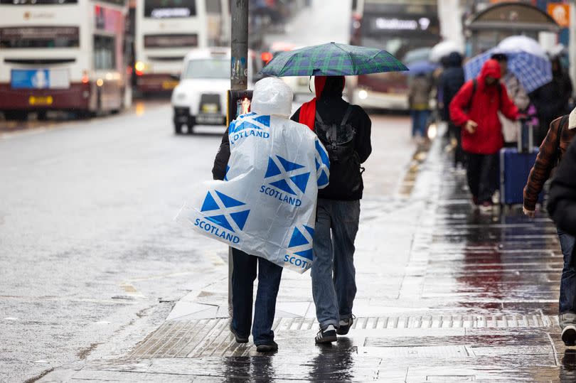 A tourist wearing a poncho featuring national flags of Scotland passes along a road in Edinburgh.