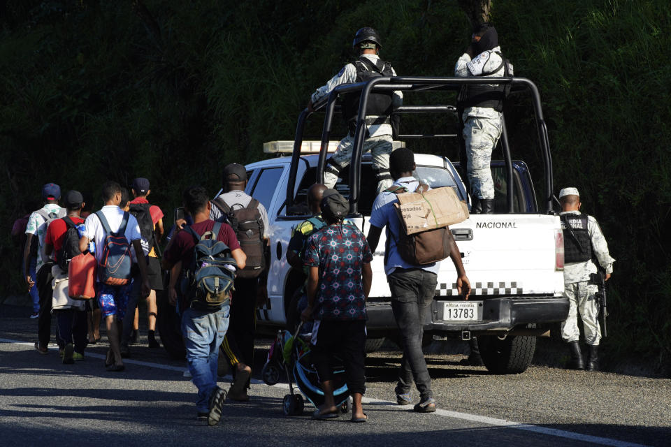 Migrants, mostly from Central America, walk past National Guard as they walk north along a coastal highway on the outskirts of Huixtla, Chiapas state, Mexico, Monday, Oct. 25, 2021. The migrants had been waiting in Tapachula, on Mexico's southern border, for refugee or asylum papers that might allow them to travel but grew tired of delays in the process and left. (AP Photo/Marco Ugarte)