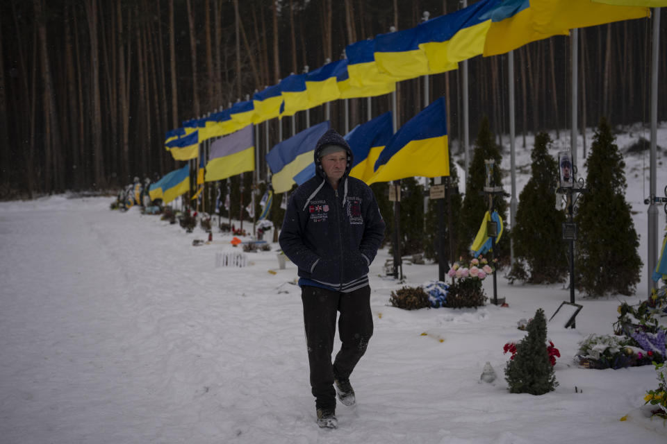 An undertaker walks by the Alley of Heroes at the Irpin Cemetery in Ukraine, Monday, Feb. 6, 2023. (AP Photo/Daniel Cole)