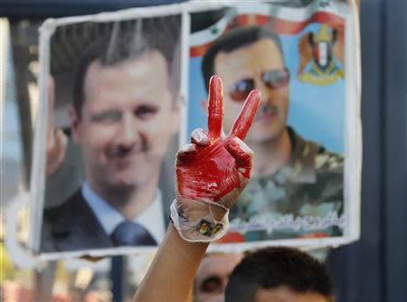 A supporter of Syria's President Bashar al-Assad gestures while wearing a glove with fake blood in front of pictures of Assad during a sit-in near the U.S. embassy in Awkar, north of Beirut, against potential U.S. strikes on Syria September 6, 2013. REUTERS/Mohamed Azakir