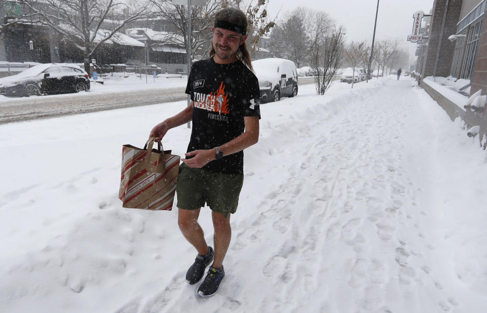 Ryan Lusk, a native of Duluth, Miin., who nows lives in Denver, heads out of a grocery store with his purchases as a storm packing snow and high winds sweeps in over the region Tuesday, Nov. 26, 2019, in Denver. Stores, schools and government offices were closed or curtailed their hours while on another front, Thanksgiving Day travellers were forced to wrestle with snow-packed roads and flight delays or cancellations throughout the intermountain West. (AP Photo/David Zalubowski)