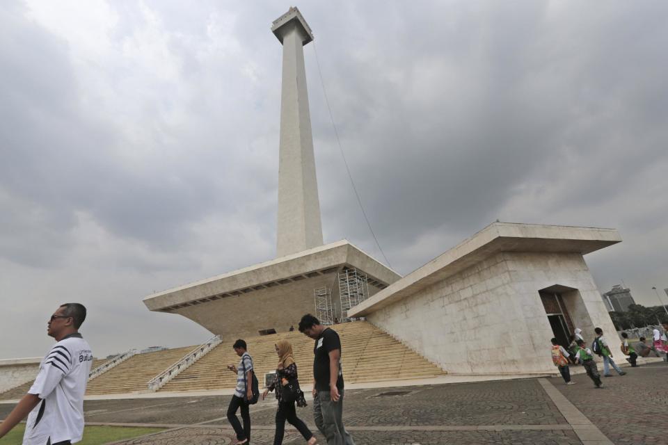 In this Thursday, May 8, 2014 photo, visitors walk past the National Monument in Jakarta, Indonesia. The 132-meter (433-feet) tall monument, a popular landmark in the capital, is being cleaned for the first time in more than two decades. (AP Photo/Dita Alangkara)